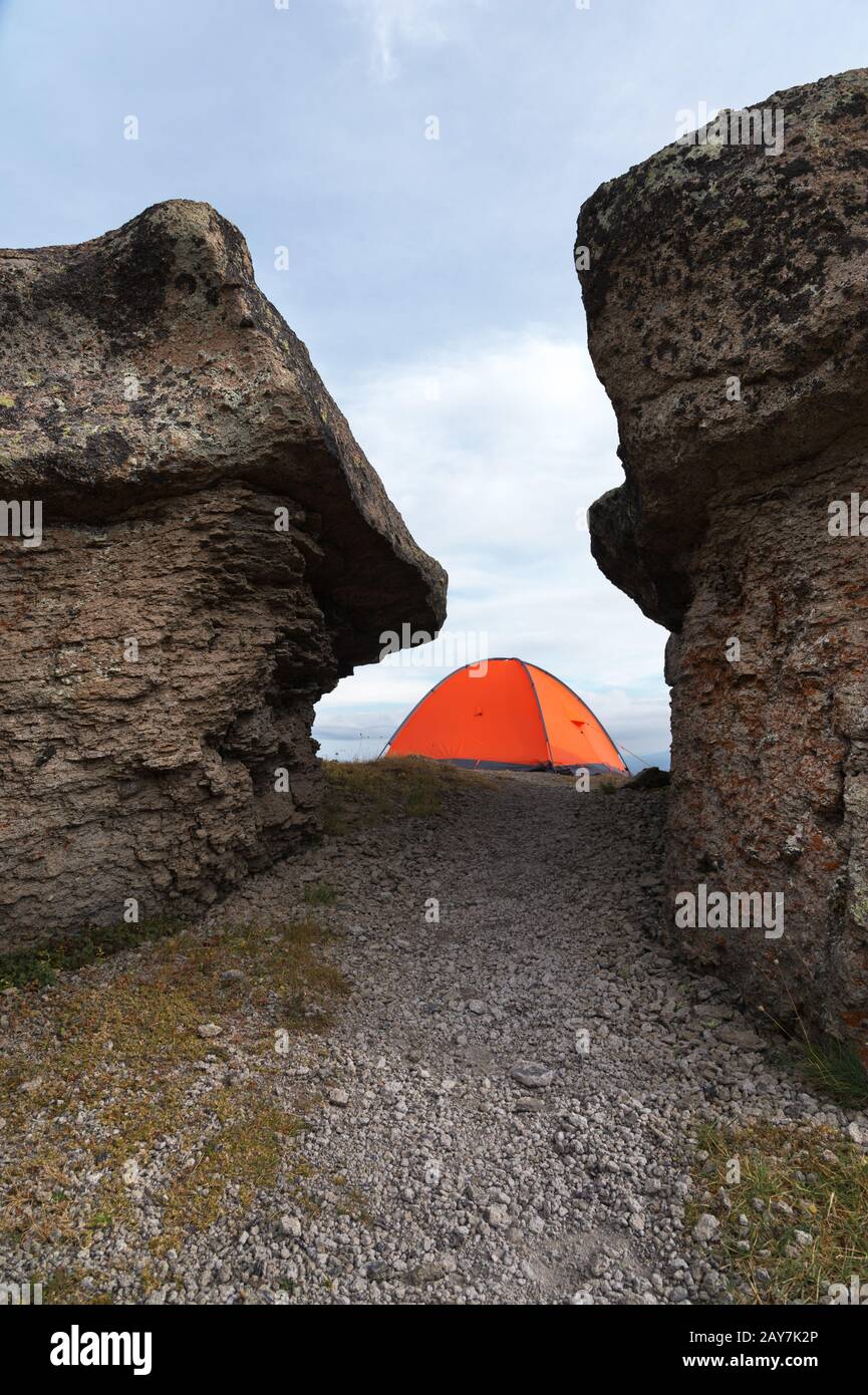 Ein orangefarbenes Zelt steht hoch in den Bergen zwischen zwei hohen Felsen Stockfoto