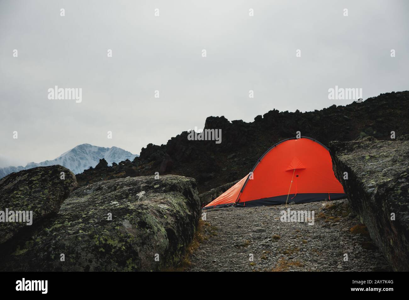 Ein orangefarbenes Zelt steht hoch in den Bergen zwischen zwei hohen Felsen Stockfoto