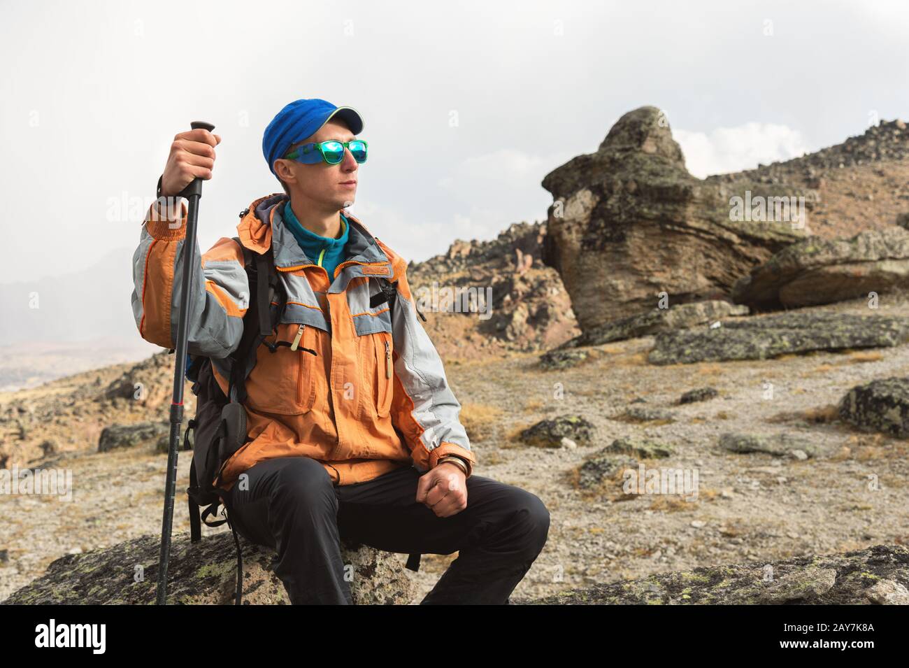 Ein einsamer Tourist mit Rucksack und Sonnenbrille ruht auf einem Felsen Stockfoto