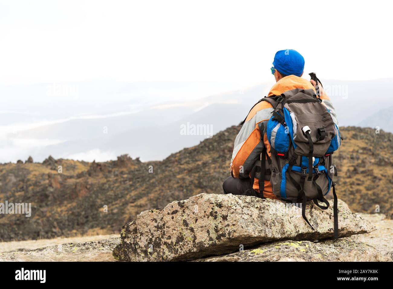 Ein einsamer Tourist mit Rucksack und Sonnenbrille ruht auf einem Felsen Stockfoto