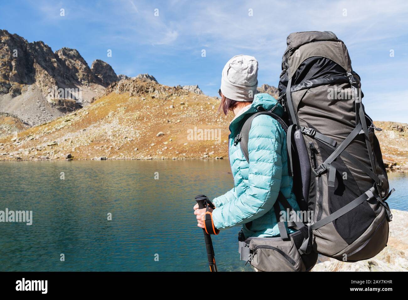 Ein Wandermädchen in Sonnenbrille und ein Hut mit Rucksack und Bergausrüstung mit aufspürbaren Trecks in den Händen blickt auf das schöne V Stockfoto