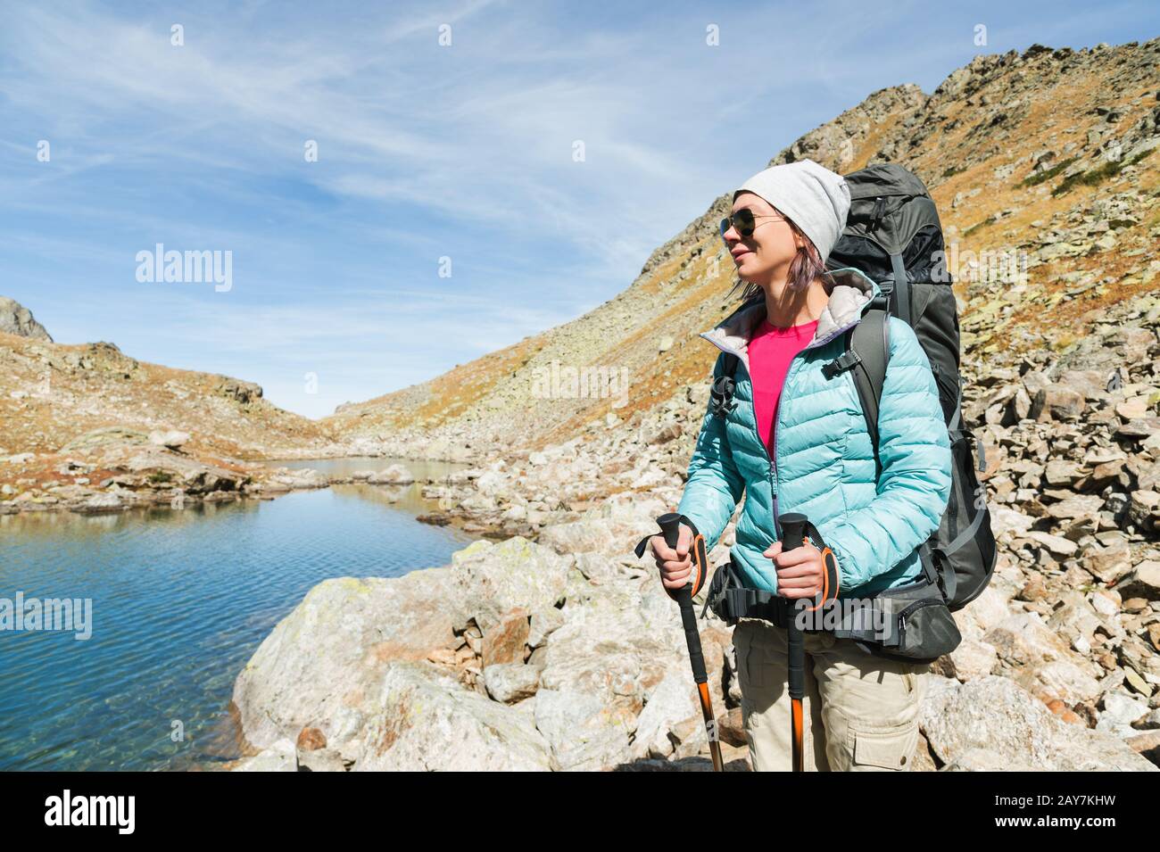 Ein Wandermädchen in Sonnenbrille und ein Hut mit Rucksack und Bergausrüstung mit aufspürbaren Trecks in den Händen blickt auf das schöne V Stockfoto