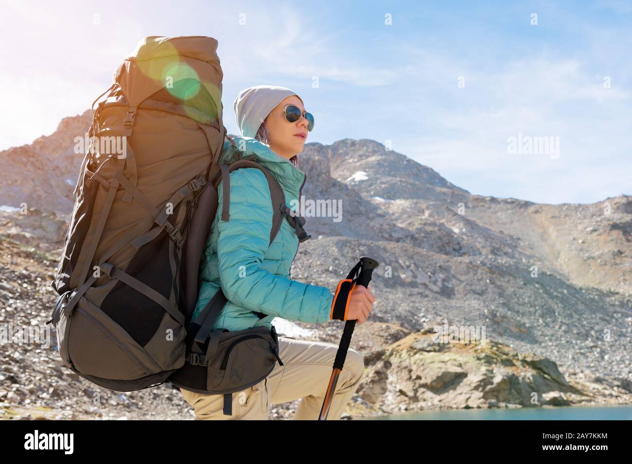 Ein Wandermädchen in Sonnenbrille und ein Hut mit Rucksack und Bergausrüstung mit aufspürbaren Trecks in den Händen blickt auf das schöne V Stockfoto