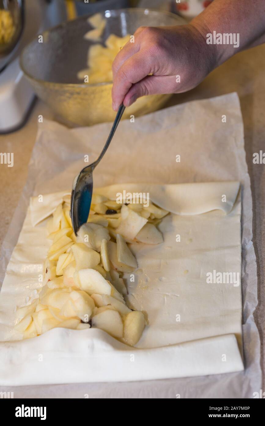 Person füllt Blätterteig mit apfelscheiben und Rosinen - Apfelstrudel Stockfoto