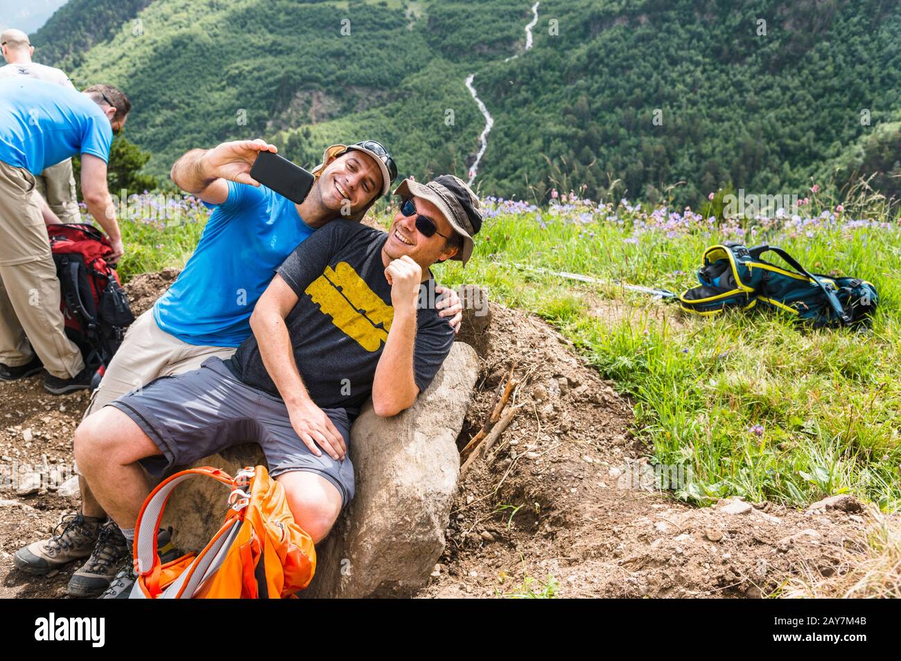 Zwei Erwachsene Männer sitzen auf einem Felsen in den Bergen und machen Selfies am Telefon Stockfoto