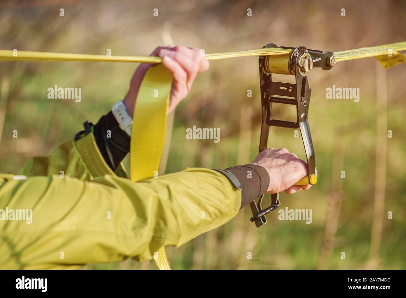 Die Hände EINES Mannes stellen eine Ausrüstung für das Slacklining auf, bevor sie verrückte Slacklining-Tricks machen und auf Slacklin in einem Park in der Natu laufen Stockfoto