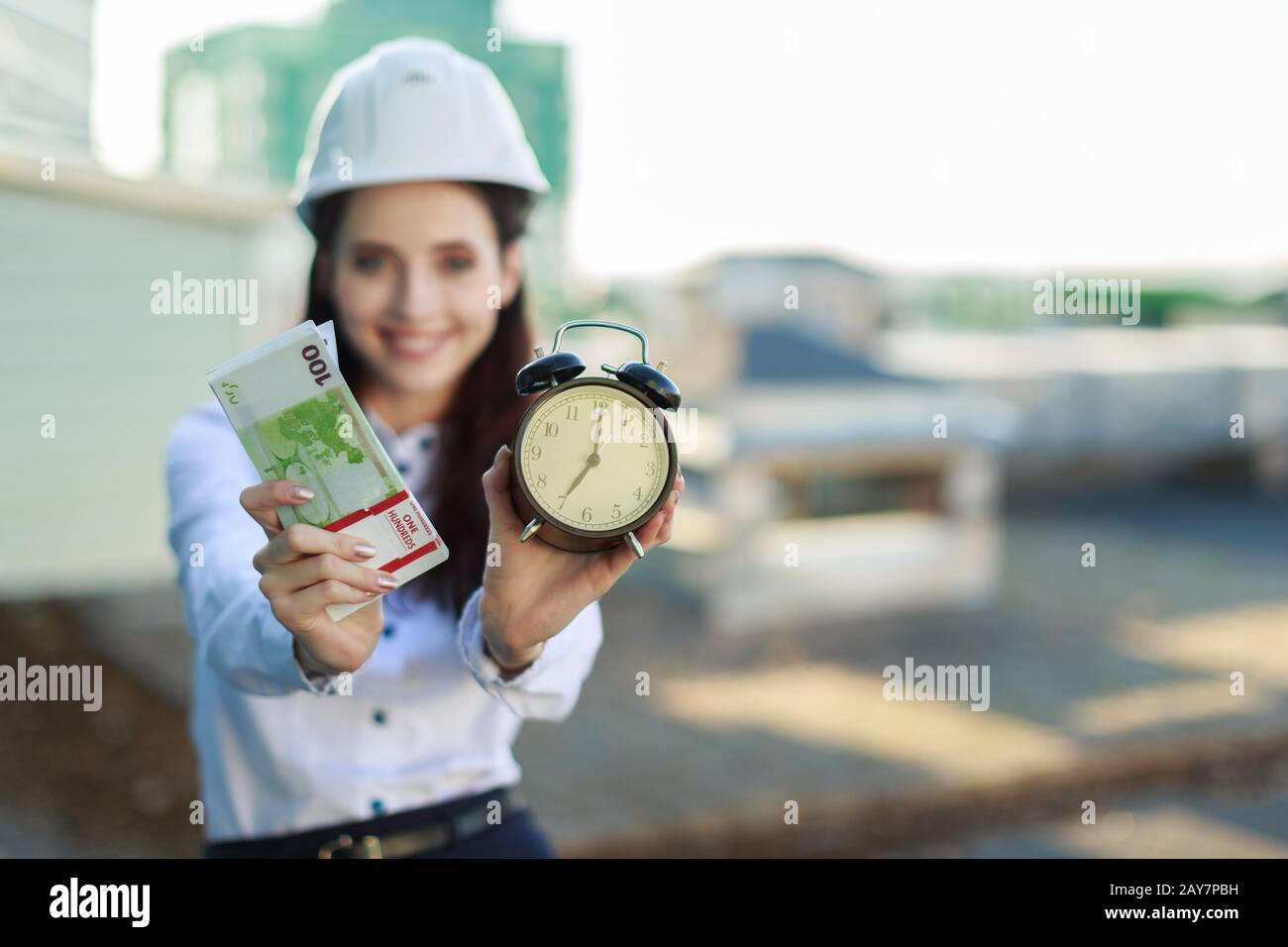 Attraktive Geschäftsfrau in weißer Bluse, Helm und schwarzem Rock stehen auf dem Dach und halten Geld und Wecker Stockfoto