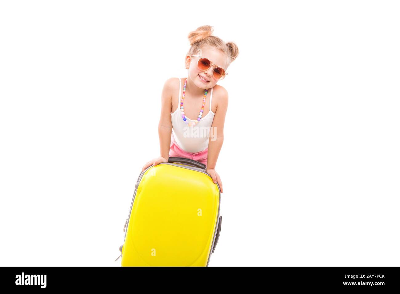 Süßes junges Mädchen in weißem Hemd, rosafarbene Shorts und Sonnenbrille stehen in der Nähe des gelben Koffers Stockfoto