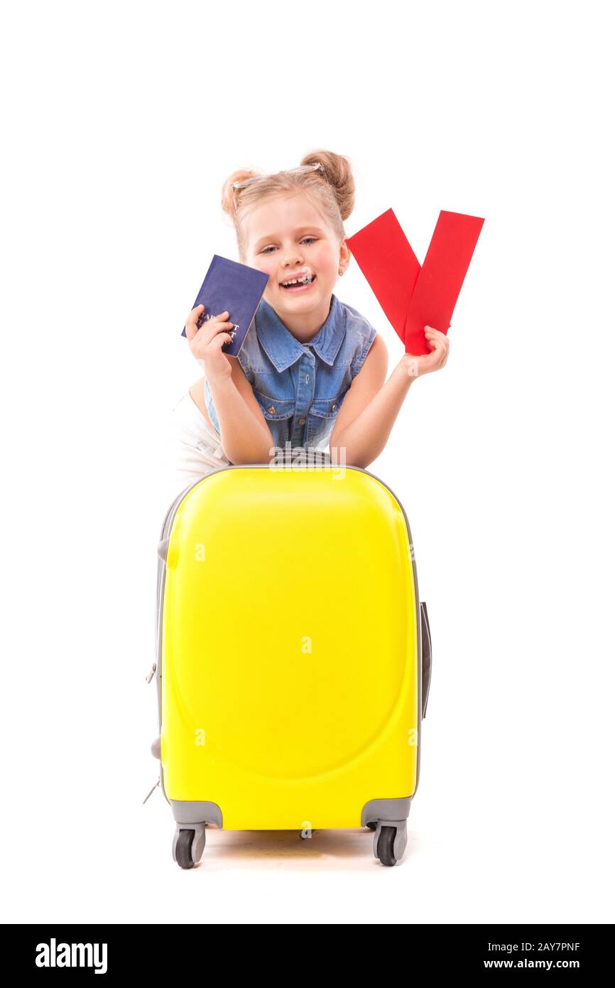 Hübsches kleines Mädchen in blauem Hemd, weiße Shorts und Sonnenbrille lehnen sich auf den gelben Koffer und halten rote Karten und Reisepass Stockfoto