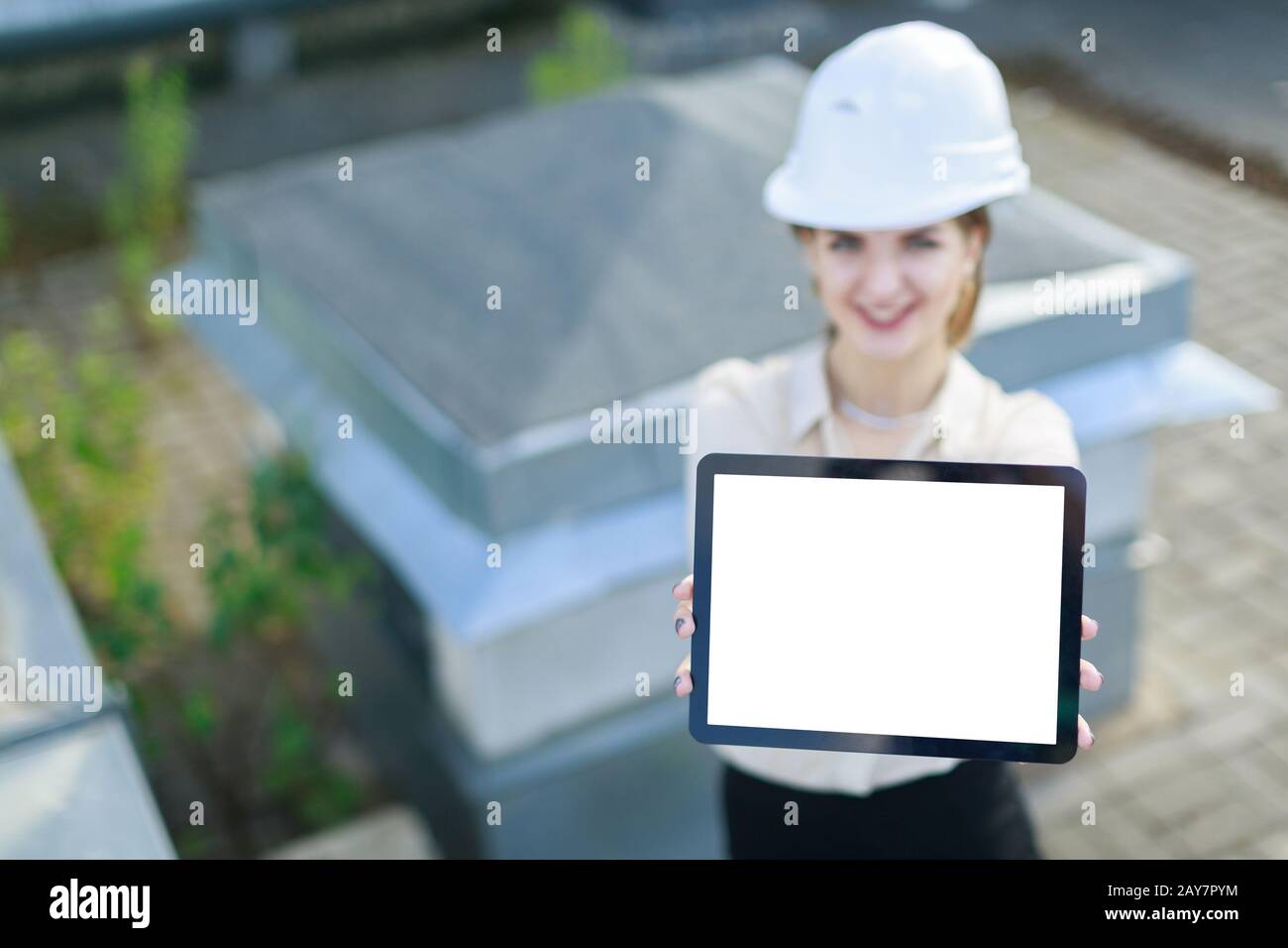 Attraktive Geschäftsfrau in weißer Bluse, Armbanduhr, Helm und schwarzem Rock stehen auf dem Dach und zeigen leere Tablette Stockfoto