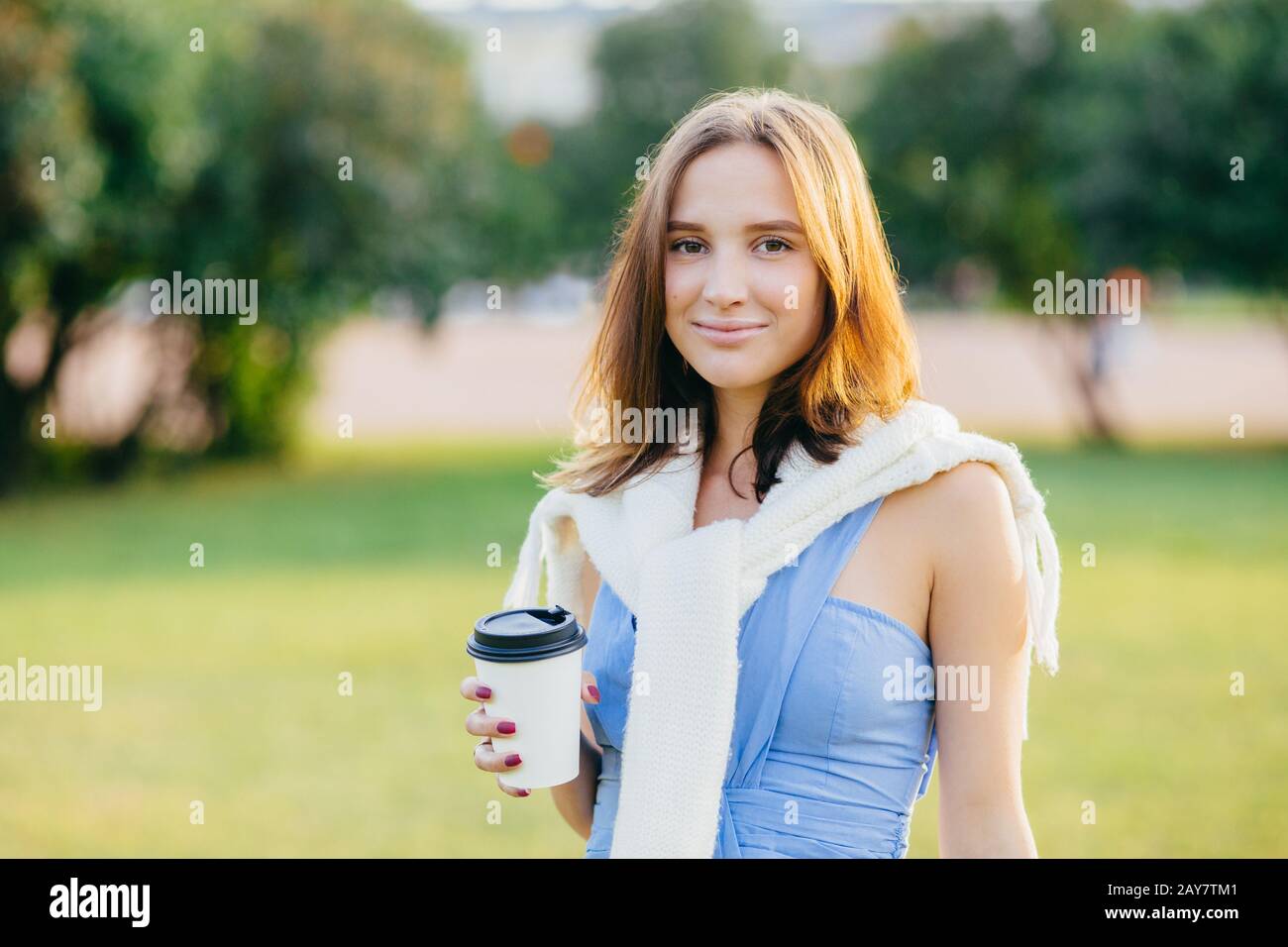 Außenaufnahmen von hübsch aussehenden jungen europäischen Frauen mit dunklem Haar, Kaffee zum Mitnehmen, Freizeit im Park, legere T-Shirts und Schweiß Stockfoto
