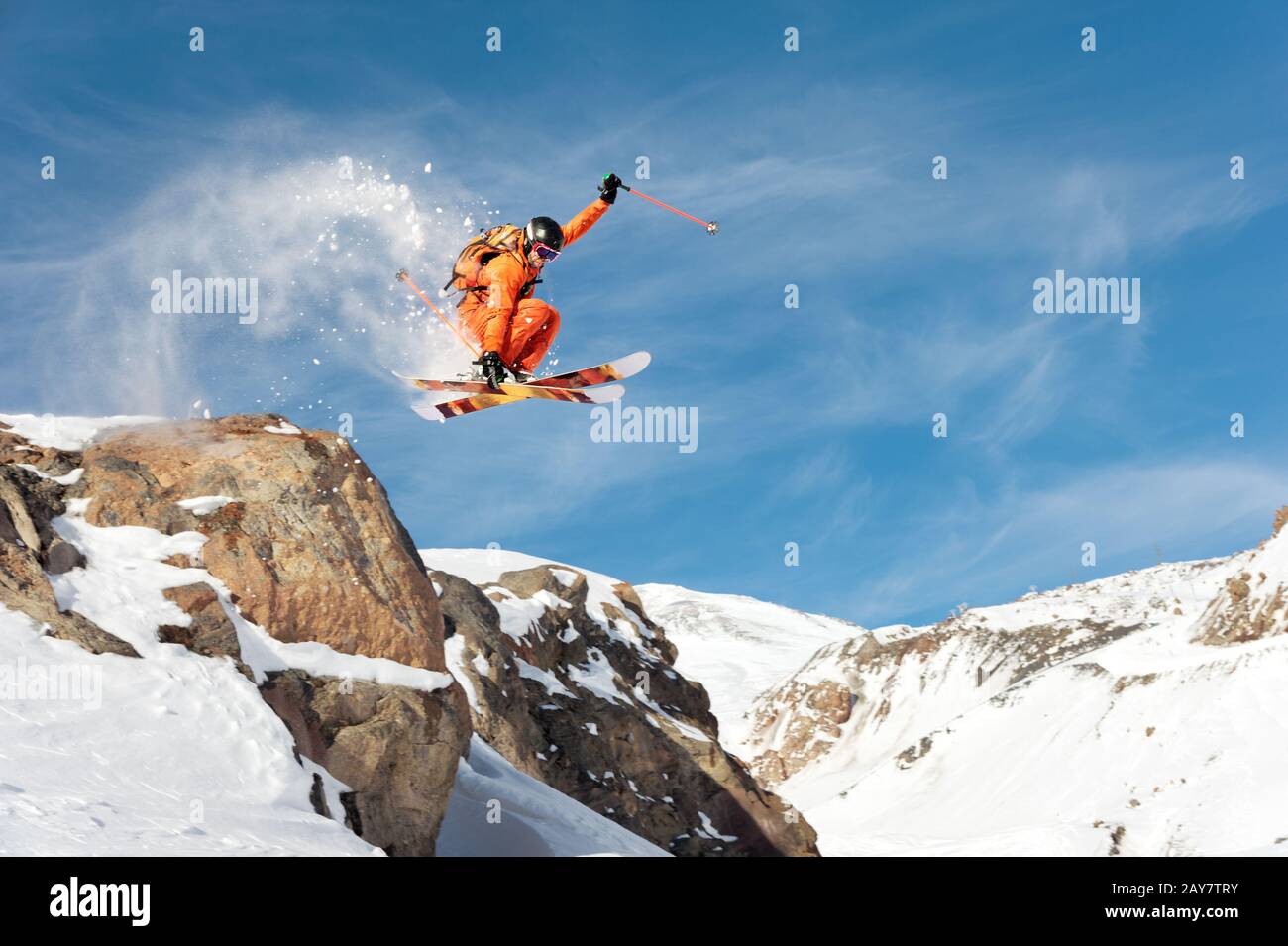 Ein professioneller Skifahrer macht einen Sprung von einer hohen Klippe gegen einen blauen Himmel und hinterlässt eine Spur von Schneepulver in den Bergen Stockfoto