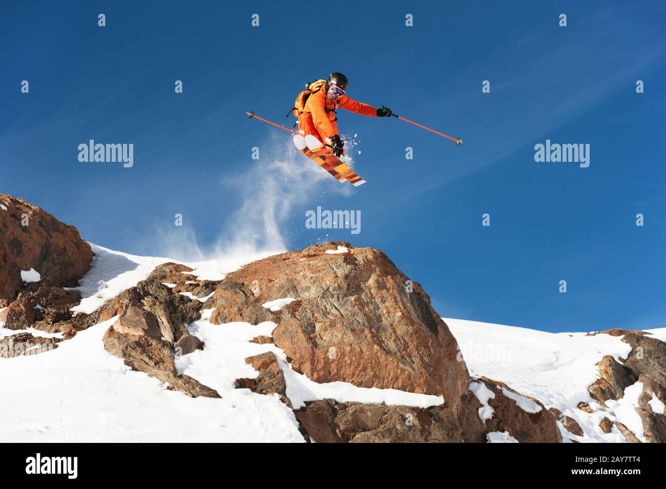 Ein professioneller Skifahrer macht einen Sprung von einer hohen Klippe gegen einen blauen Himmel und hinterlässt eine Spur von Schneepulver in den Bergen Stockfoto