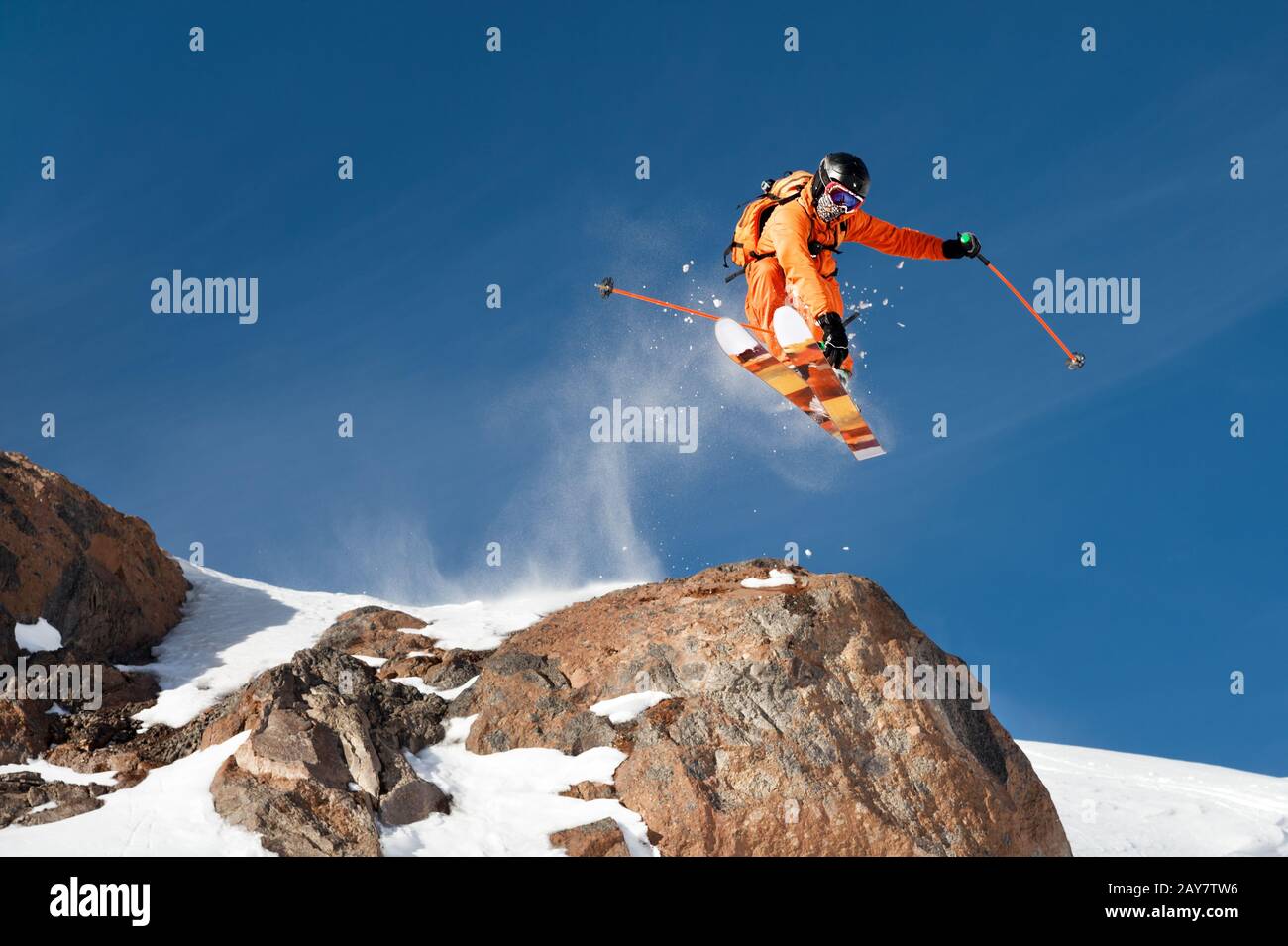 Ein professioneller Skifahrer macht einen Sprung von einer hohen Klippe gegen einen blauen Himmel und hinterlässt eine Spur von Schneepulver in den Bergen Stockfoto