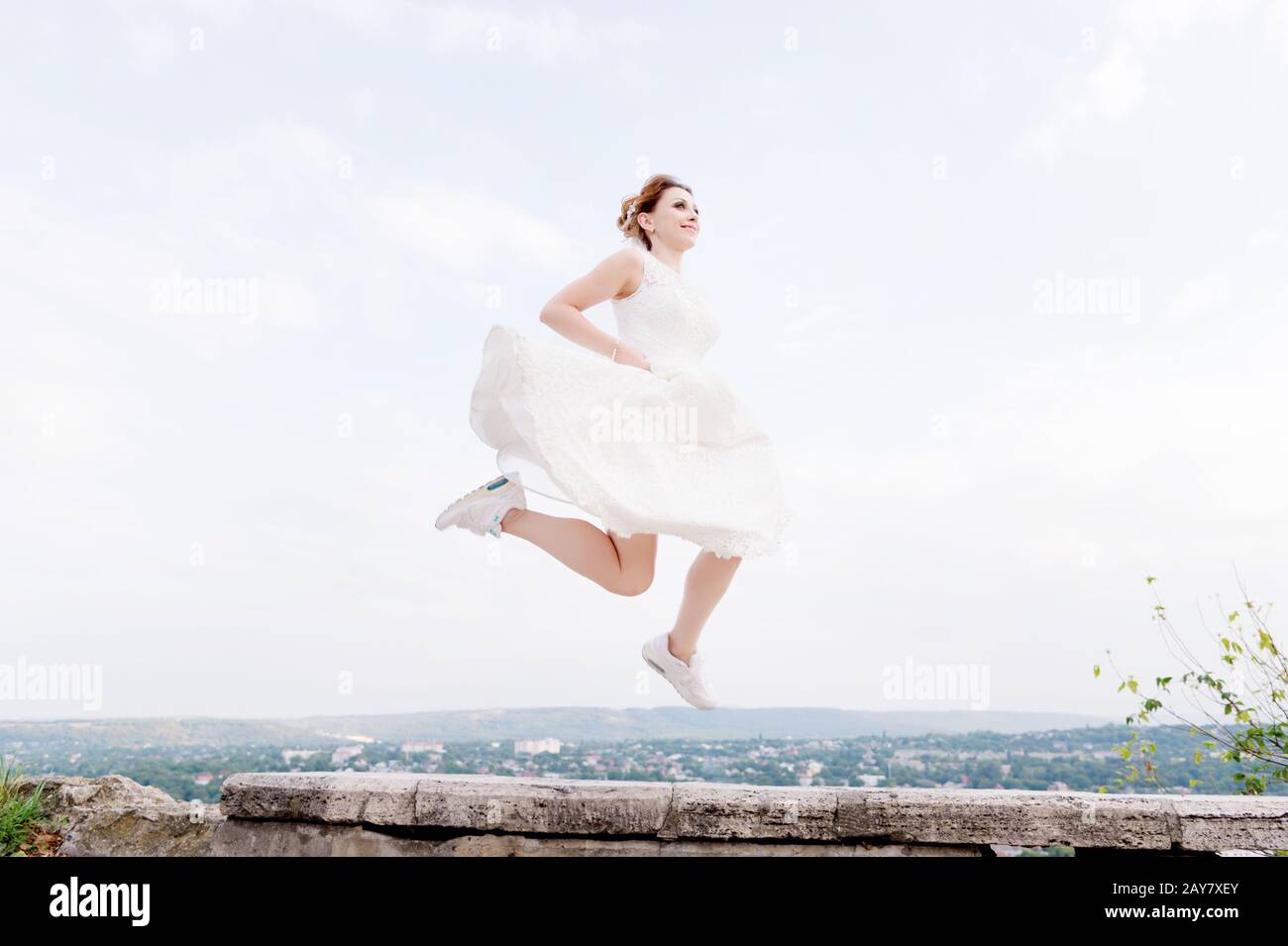 Vor dem Hintergrund des Stadtbildes einer kleinen Erholungsstadt im Nordkaukasus springt und hängt die verrückte Brautpast in den Himmel Stockfoto