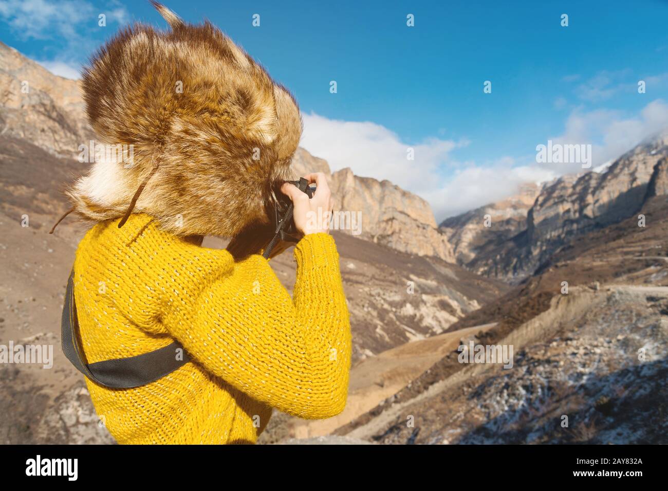 Eine Fotografin im Fellhut und ein gelber Pullover in den Bergen fotografiert auf ihrer Digitalkamera. Stockfoto