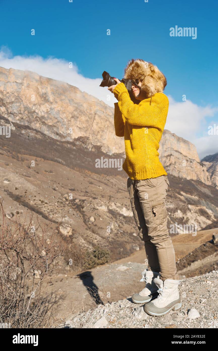 Eine Fotografin im Fellhut und ein gelber Pullover in den Bergen fotografiert auf ihrer Digitalkamera. Stockfoto