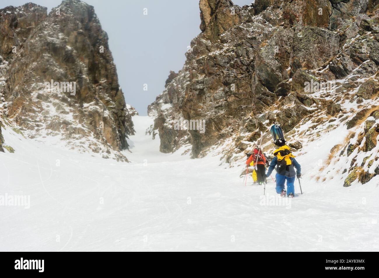 Extreme Skifahrer klettern auf den Gipfel entlang des Couloirs zwischen den Felsen vor dem Abstieg des Freeride-Rücklandes Stockfoto