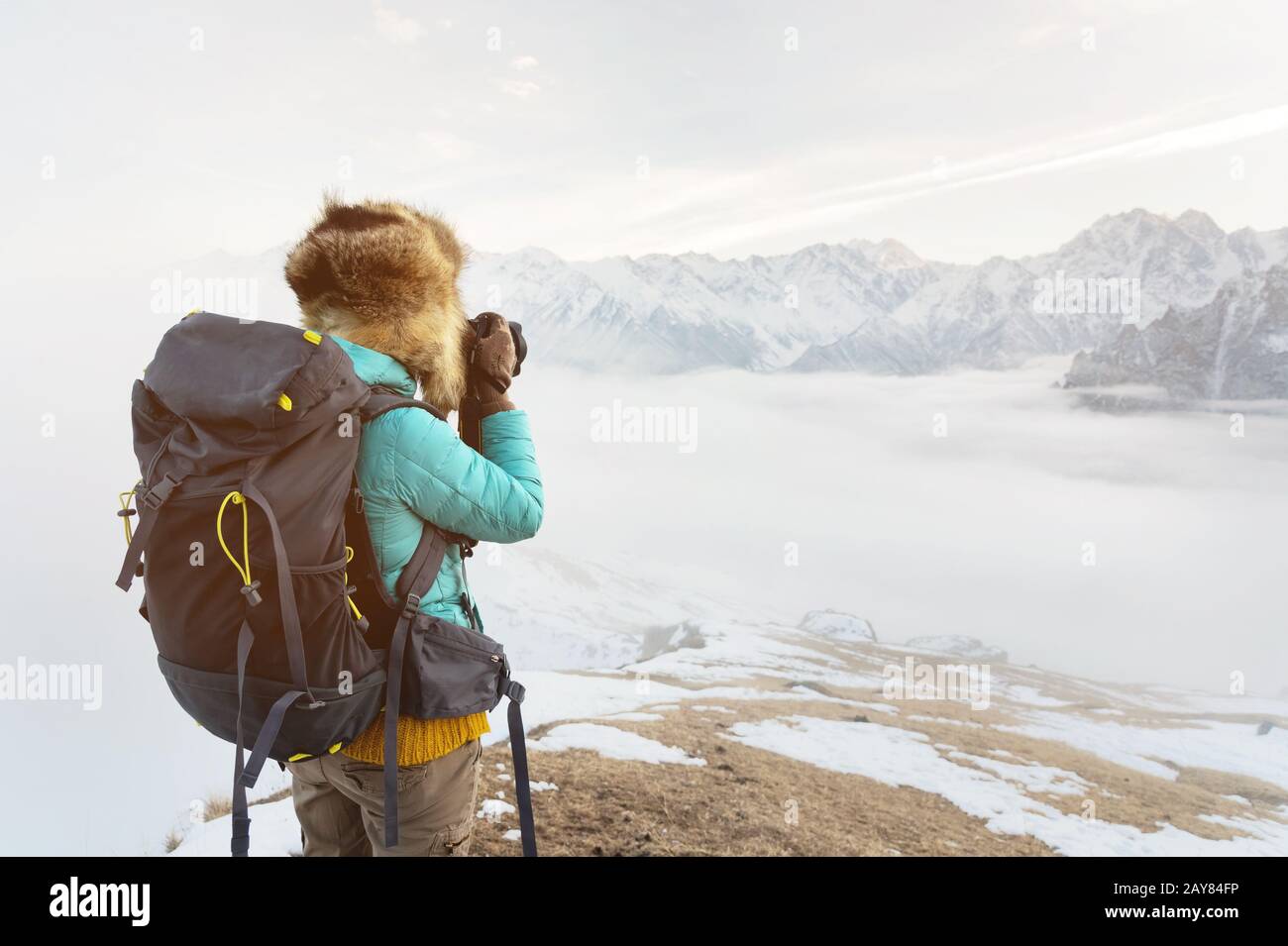 Das Porträt eines süßen Touristenmädchens in einem großen Fellhut fotografiert auf ihrer Digitalkamera in den Bergen. Stockfoto