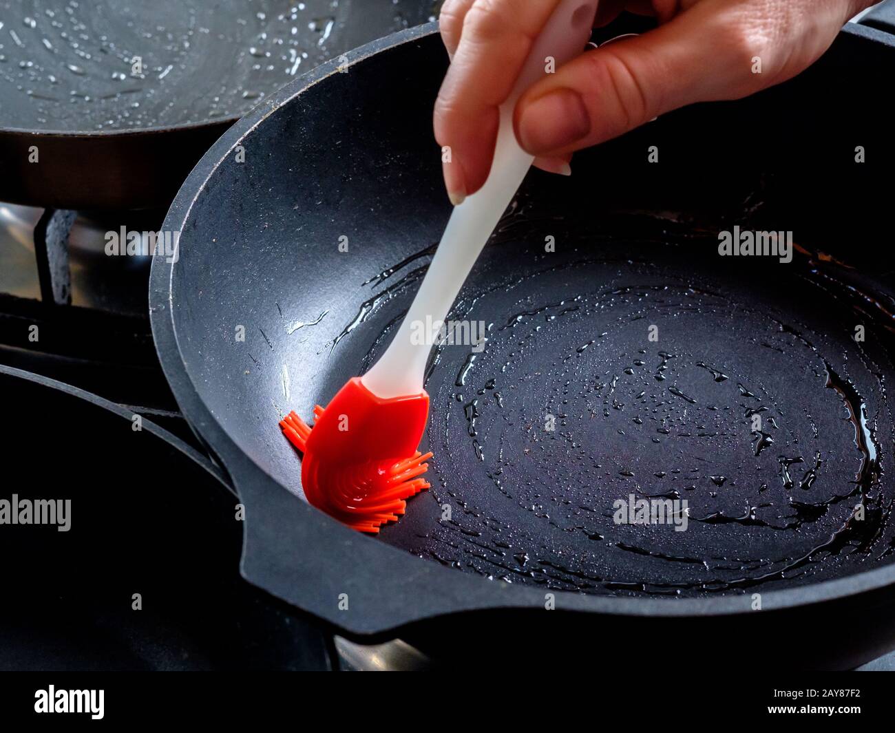 Menschliche Hand, die eine rot-heiße Pfanne mit einer roten  Silikon-Küchenbürste ölt. In der Hausküche Pfannkuchen backen.  Traditioneller Leckerbissen für den Urlaub o Stockfotografie - Alamy