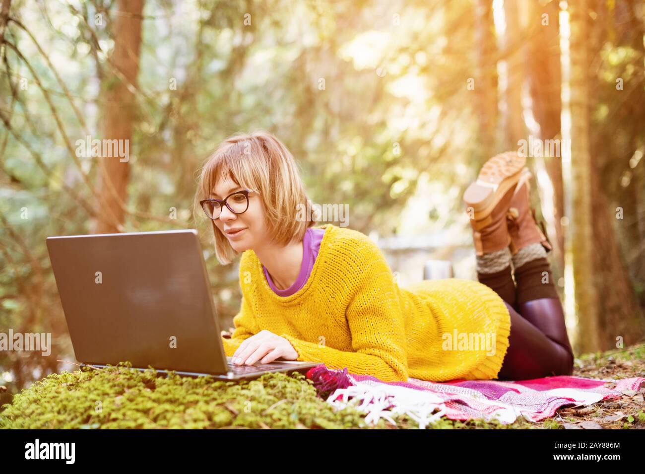 Gezautes Bild eines freiberuflichen Mädchen-Porträts in einem gelben Pullover und einer Brille, die nachdenklich auf den Laptop-Bildschirm in der Natur blickt Stockfoto