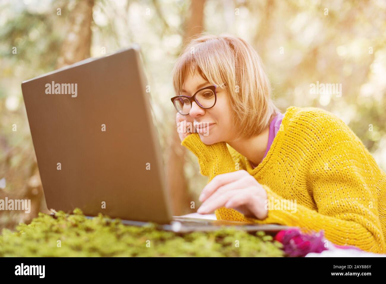 Nahaufnahmen eines freiberuflichen Mädchen-Portraits in einem gelben Pullover und einer Brille, die nachdenklich auf dem Laptop-Bildschirm in aussieht Stockfoto