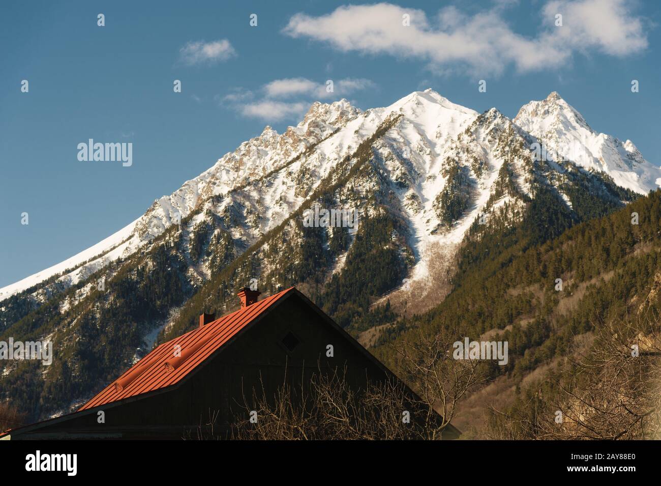 Rotes Dach eines Hauses auf dem Hintergrund eines Berges mit schneebedecktem Gipfel. Das Konzept einer Wohnung in den Bergen. Urlaub Stockfoto