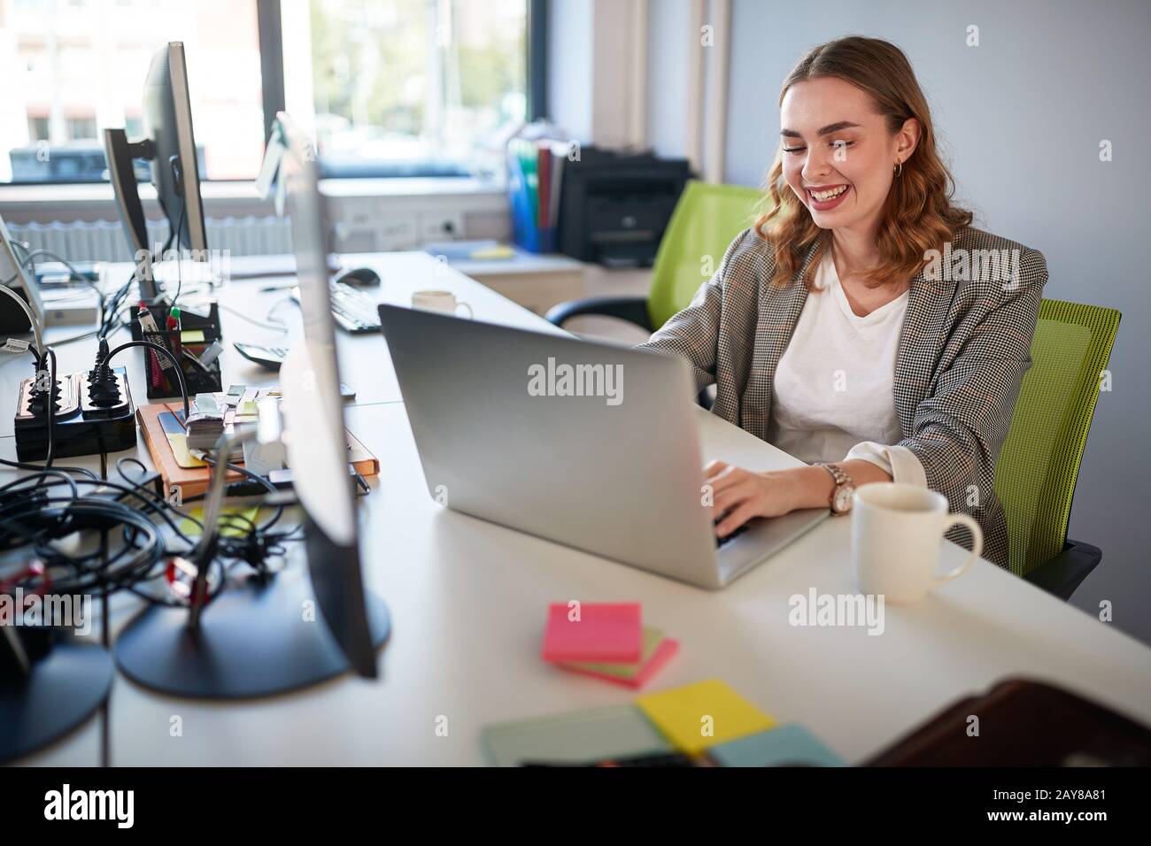 Junge Geschäftsfrau tippt am Laptop, arbeitet und lächelt. Sie liebt ihre Arbeit Stockfoto