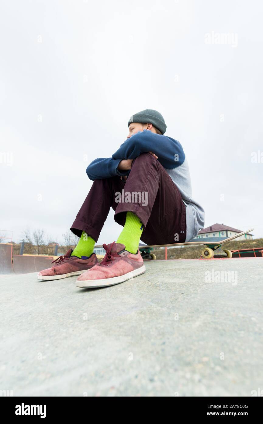 Ein Teenager sitzt auf einem Skateboard im Park. Das Konzept des Zeitvertreibs für Jugendliche in der Stadt Stockfoto