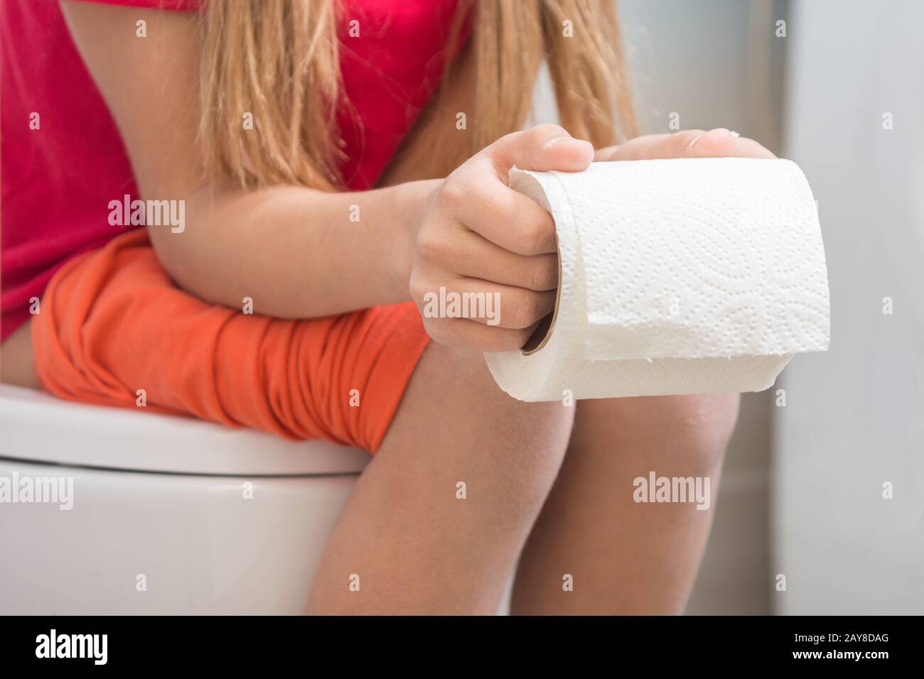 Ein Mädchen hält eine Rolle Toilettenpapier in ihren Händen, auf der Toilette sitzt Stockfoto