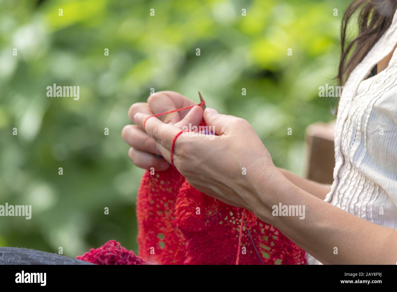 Die Hände einer Frau, die Häkelt mit roter Wolle/strickt Vor unscharfen Hintergrund Stockfoto