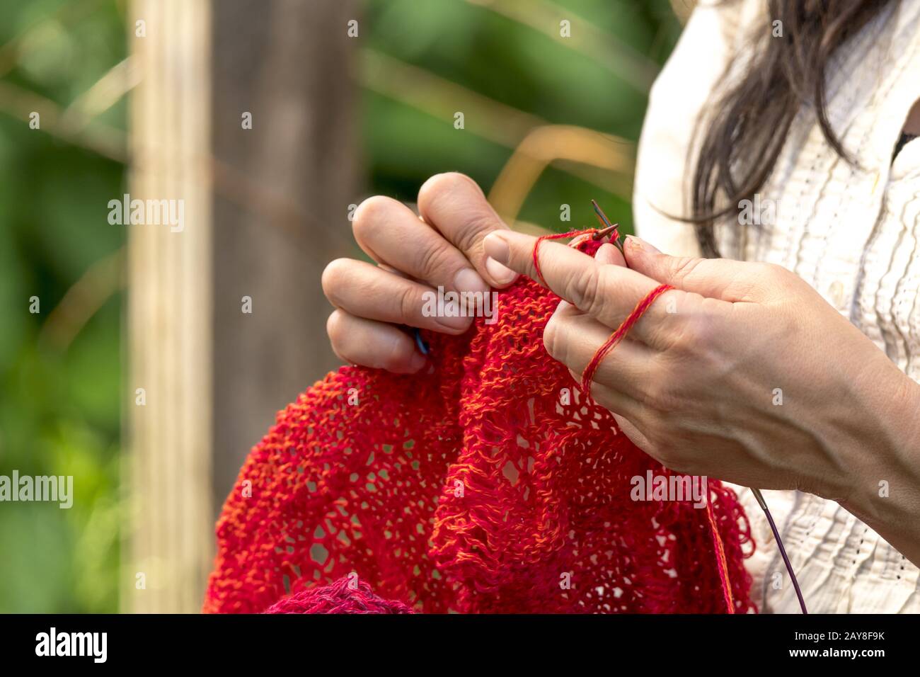 Die Hände einer Frau, die Häkelt mit roter Wolle/strickt Vor unscharfen Hintergrund Stockfoto
