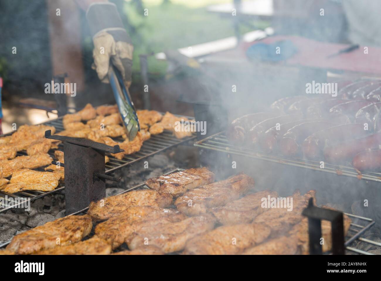 Steak und Würstchen mit Grillzangen auf den Grill stellen Stockfoto