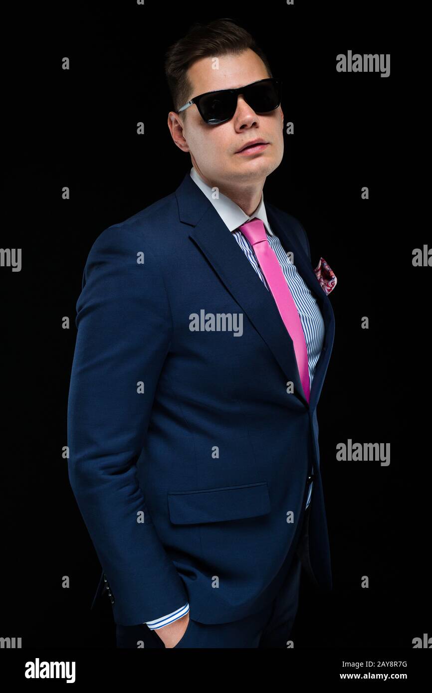 Portrait von zuversichtlich gut aussehender Geschäftsmann in Sonnenbrille auf schwarzen Hintergrund mit Händen in den Taschen Stockfoto