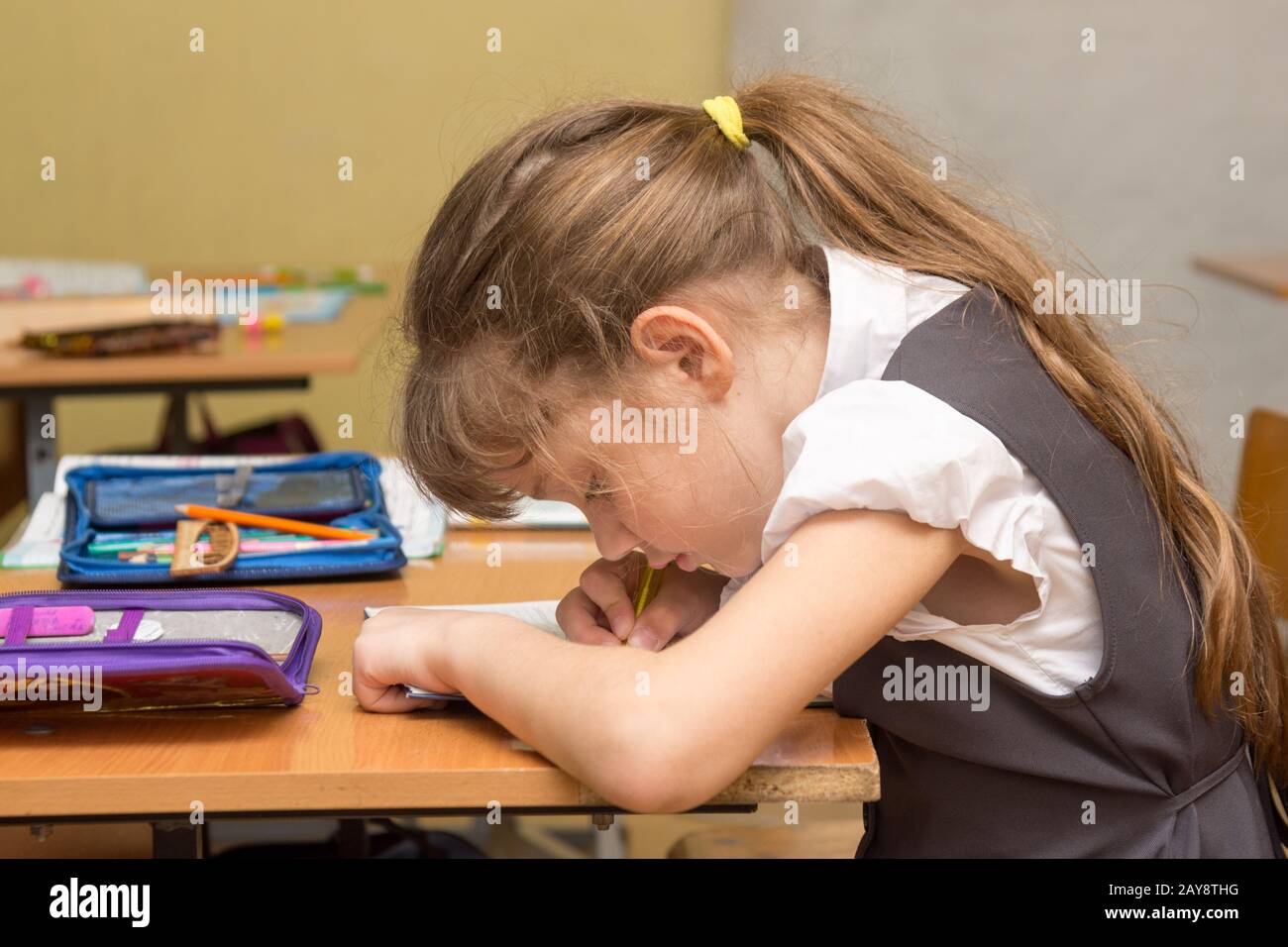 Eine Schülerin mit einer falschen Körperhaltung bei der Lektion schreibt in einem Notebook Stockfoto