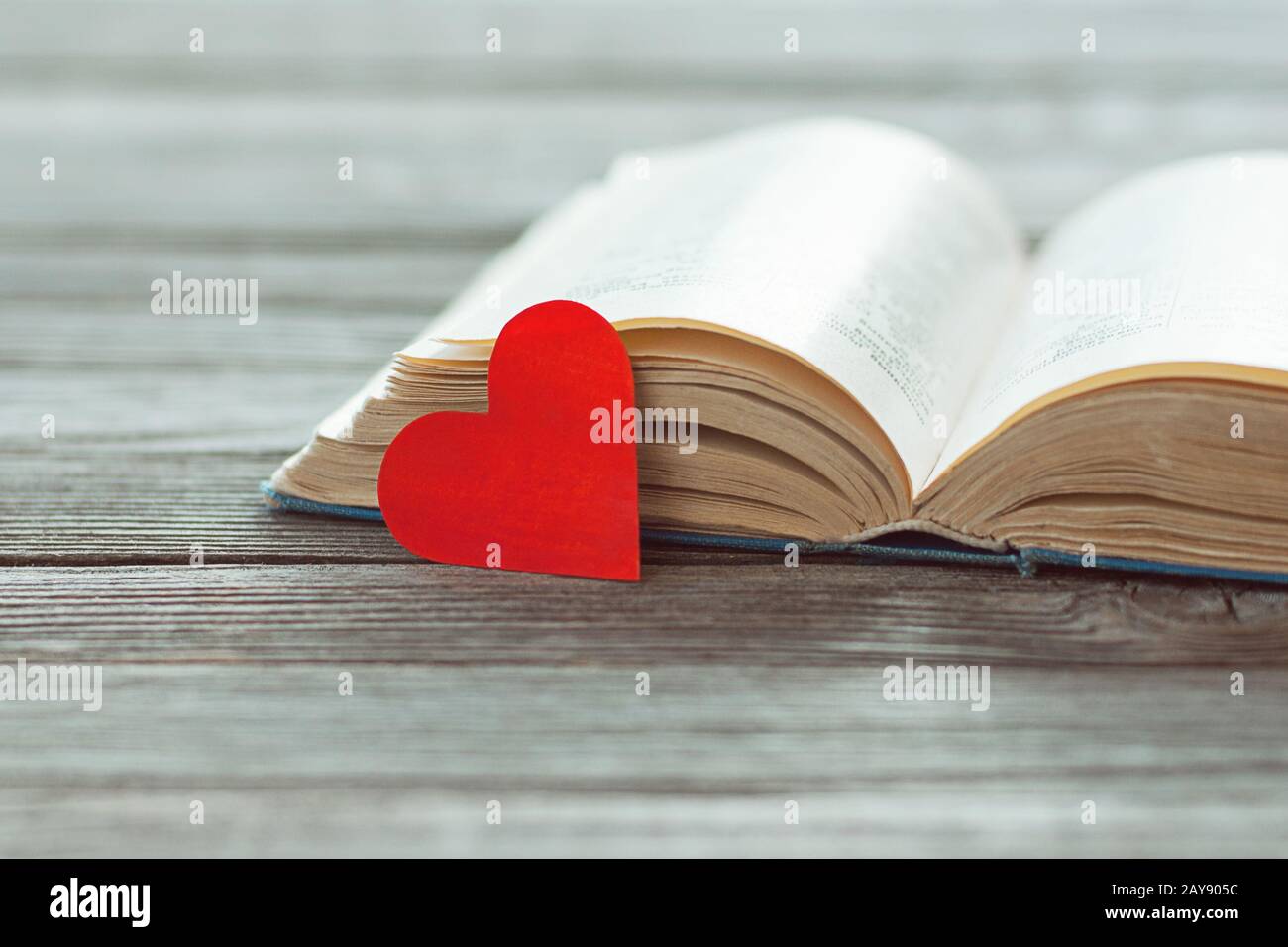 Öffnen Sie altes Buch und rotes Papierherz auf Holztisch, Poesie und Liedtext-Konzept Stockfoto