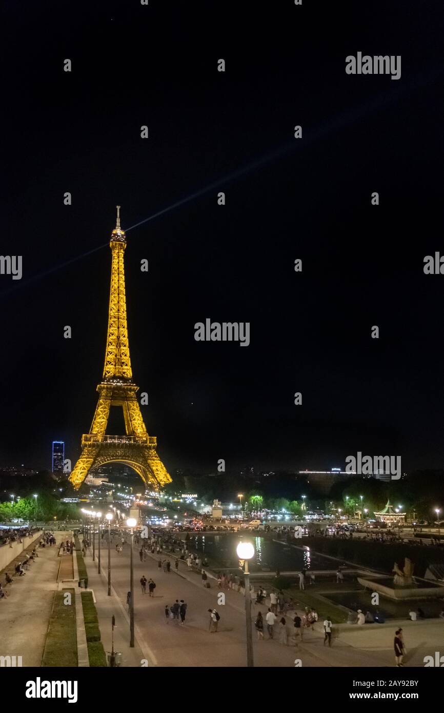 Zahlreiche Besucher schlendern an einem warmen Sommerabend durch den beleuchteten Eiffelturm in Paris. Stockfoto