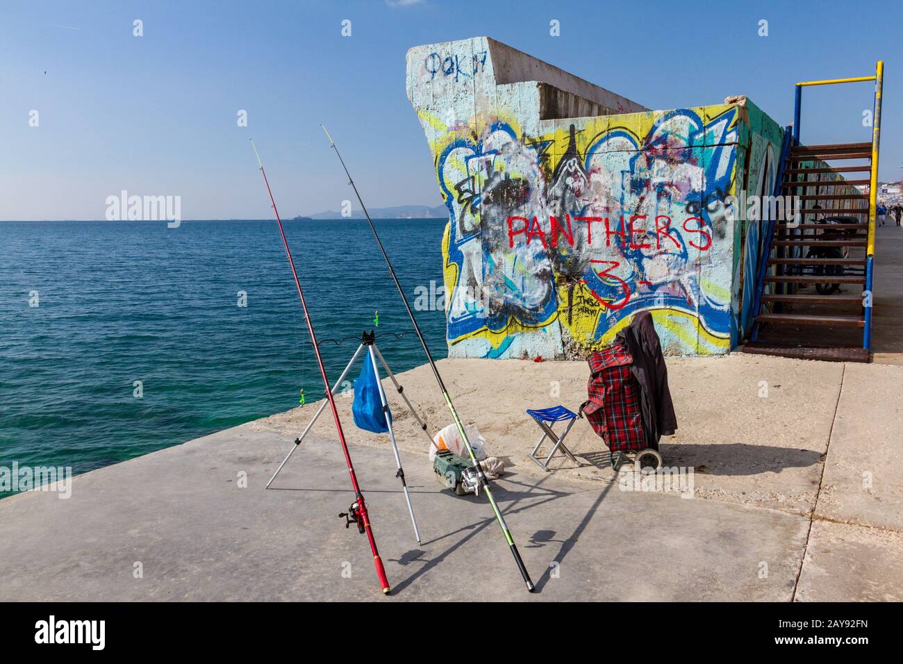 Unbeaufsichtigte Angelruten an der Promenade gegen eine Wand, die Graffiti im Palaio Faliro in Athen, Griechenland, erreicht Stockfoto