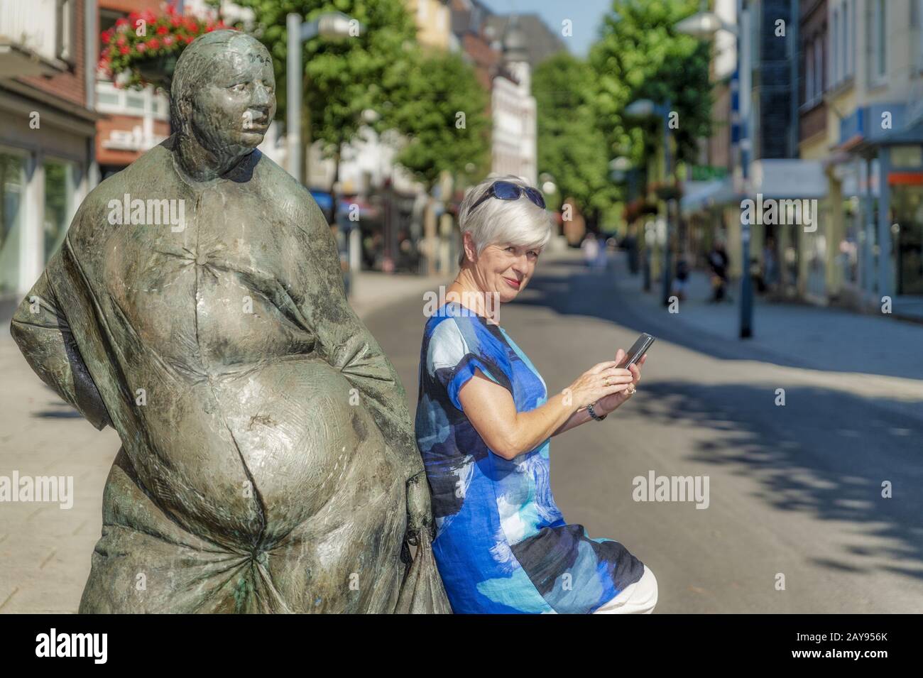 Eine Seniorin steht mit einem Smartphone in der Hand auf einer Skulptur. Stockfoto