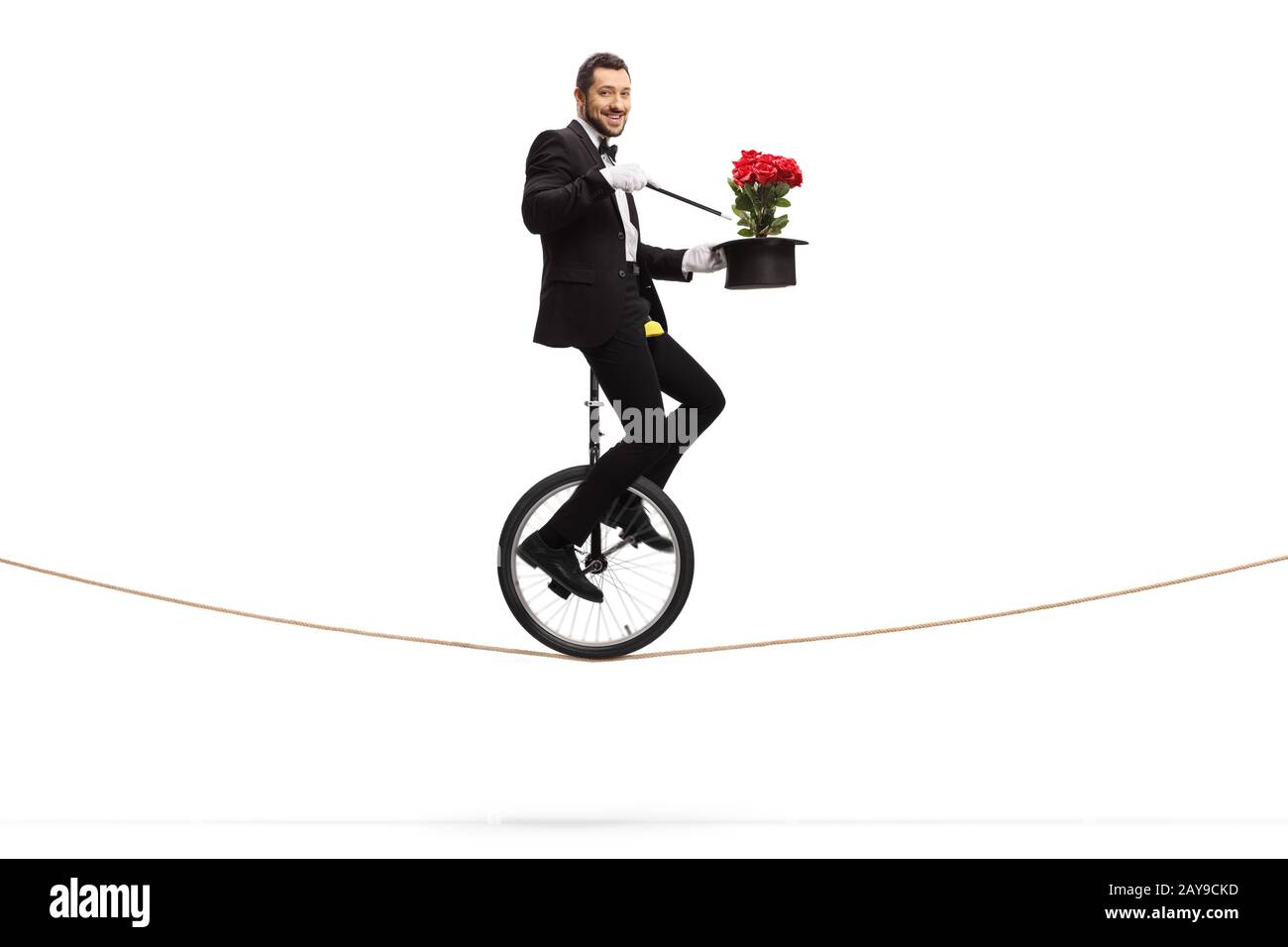 Zauberer führt einen Trick mit roten Rosen durch und reitet ein Einrad auf einem auf weißem Hintergrund isolierten Seil Stockfoto
