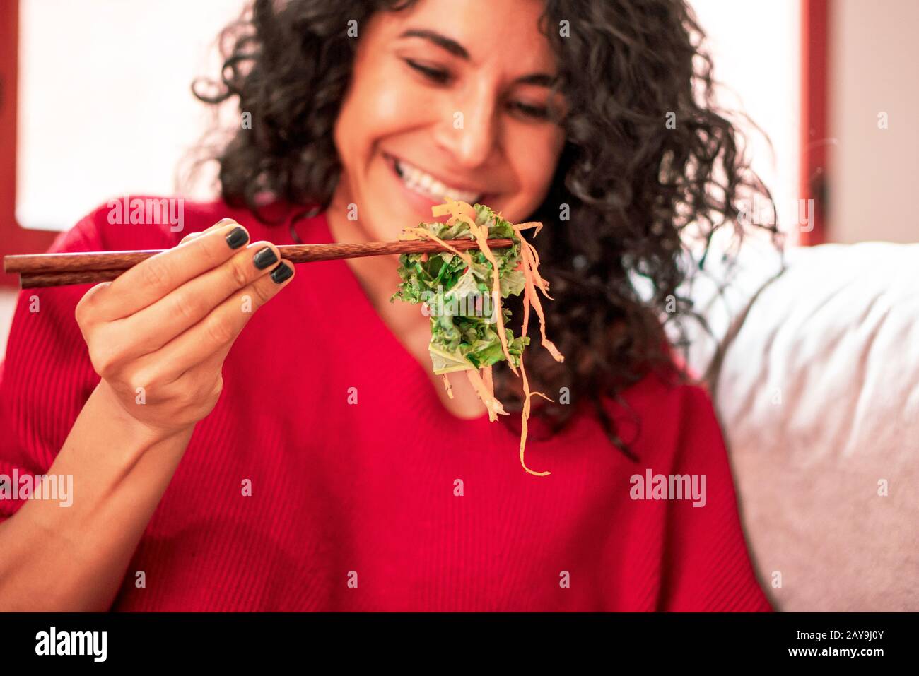 Latin Woman essen Salat, Diät mit Essstäbchen, Salat trägt Salat, Lachs, Avocado, Karotte, Zucchini, Samen und Nüsse Stockfoto