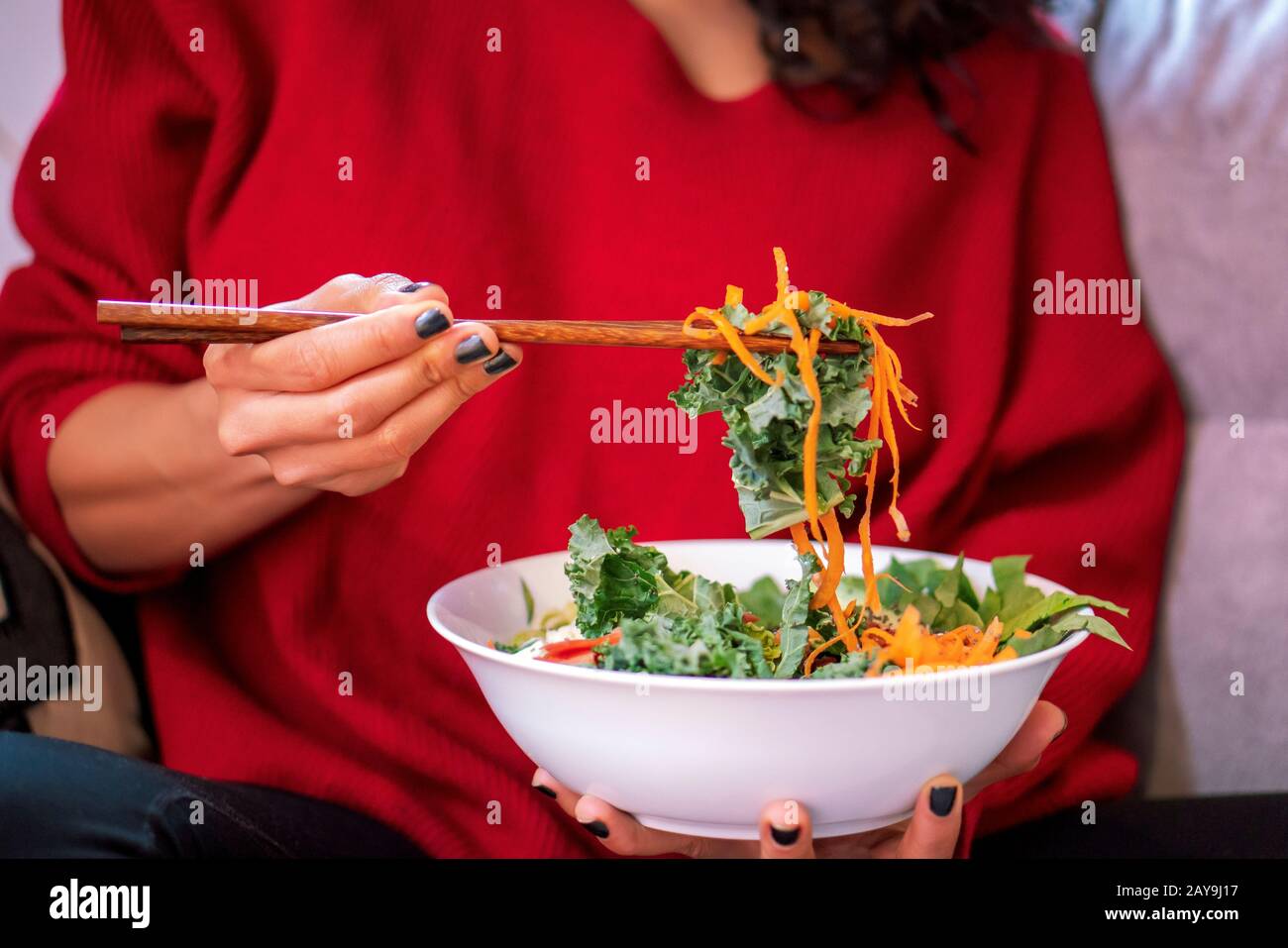 Latin Woman essen Salat, Diät mit Essstäbchen, Salat trägt Salat, Lachs, Avocado, Karotte, Zucchini, Samen und Nüsse Stockfoto