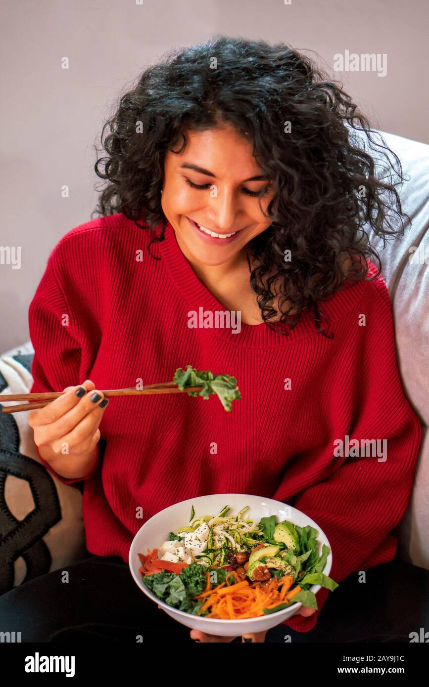 Latin Woman essen Salat, Diät mit Essstäbchen, Salat trägt Salat, Lachs, Avocado, Karotte, Zucchini, Samen und Nüsse Stockfoto