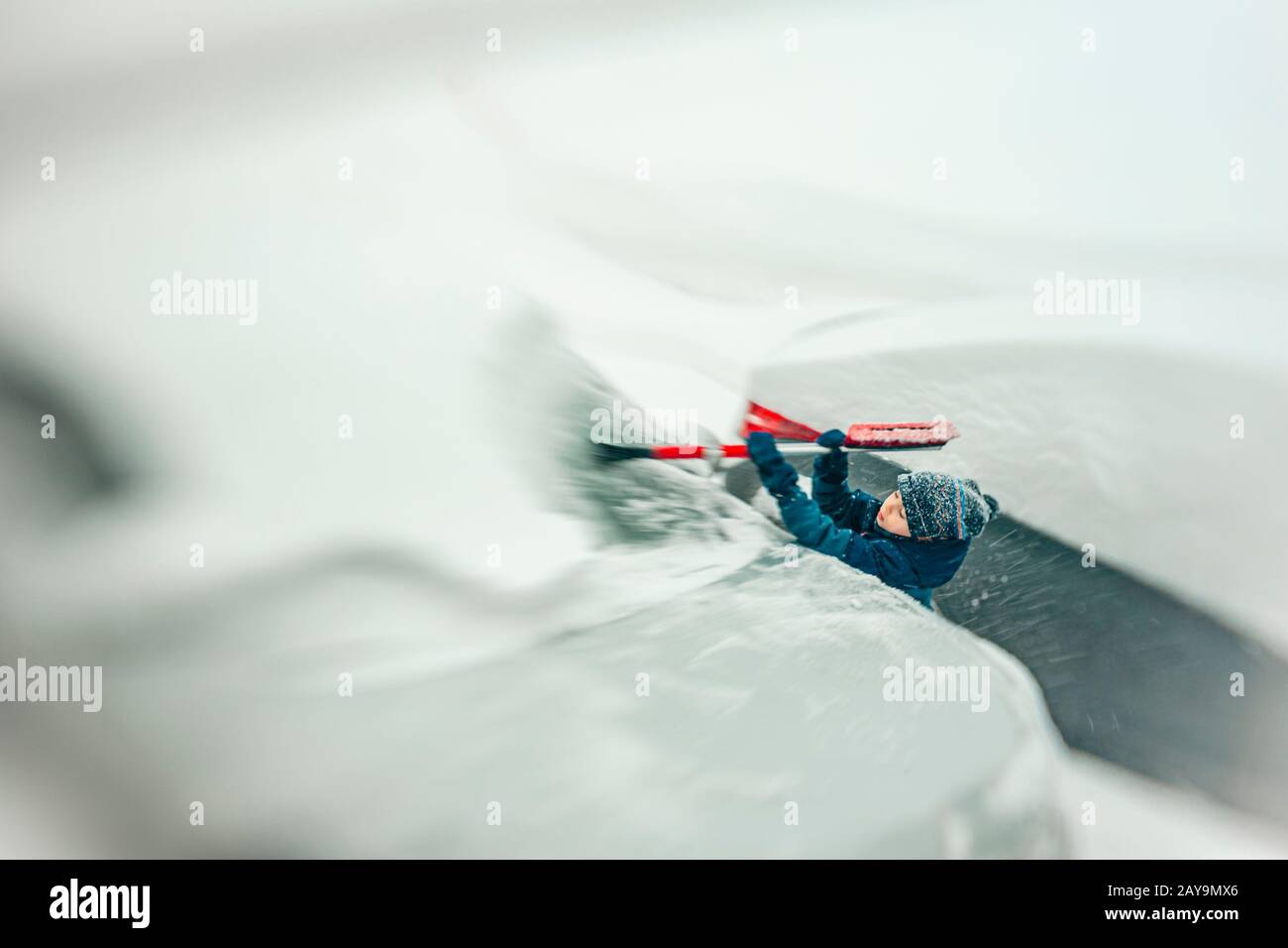 7 Jahre alter Junge, der bei einem Schneesturm Schnee von einem Auto abzieht Stockfoto