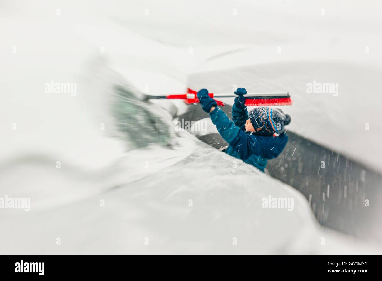 7 Jahre alter Junge nimmt den Schnee von der Windschutzscheibe während eines Schneesturms Stockfoto
