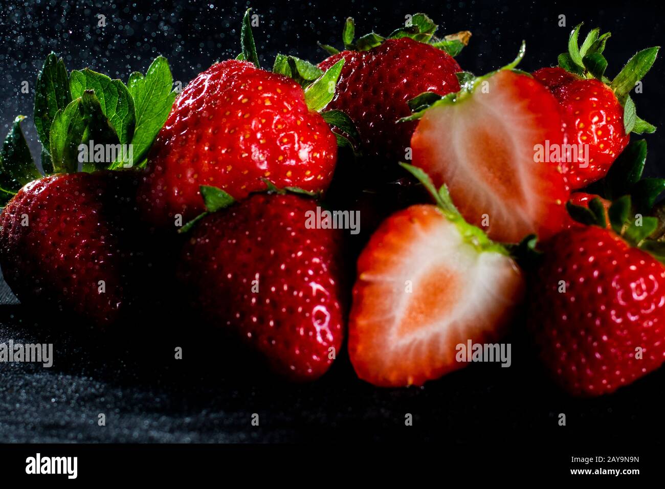 Erdbeeren mit schwarzem Hintergrund und leichtem Regen Stockfoto