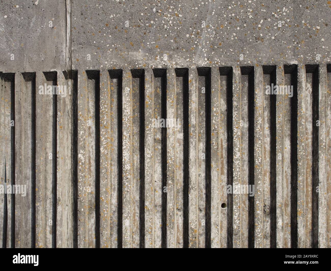 Alte Betonaußenwand mit geriffeltem, vertikalem Streifendesign mit rauer Gussstruktur und Schatten Stockfoto