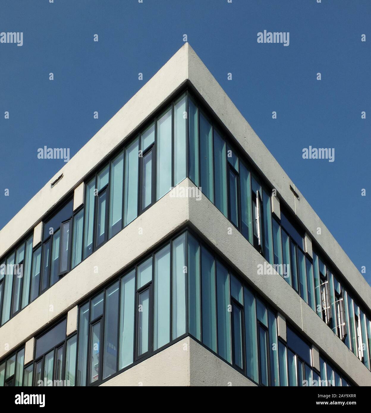 Nach oben Blick auf eine Ecke eines modernen kantigen Betonhochweißen Bürogebäudes mit hellem Himmel Stockfoto