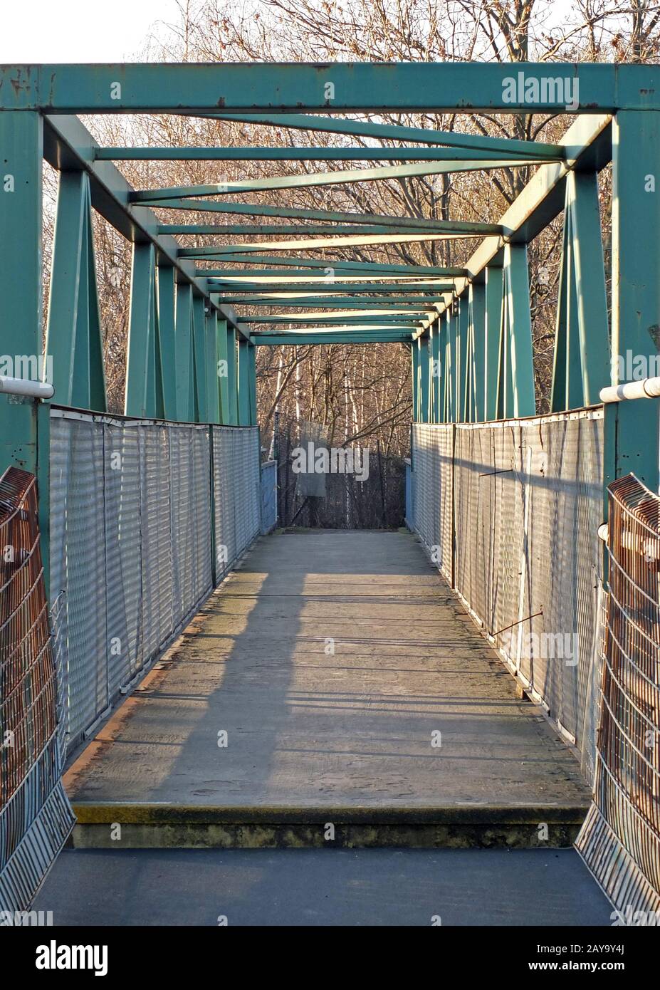 Eine perspektivische Ansicht entlang einer grünen, rostenden Fußgängerbrücke aus Metall mit Schienen und Trägern Stockfoto