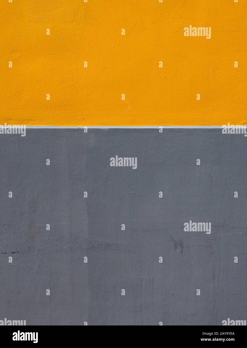 Gelbe und graue Farbbereiche auf einer rauen, strukturierten Betonwand, die durch einen horizontalen weißen Streifen geteilt wird Stockfoto